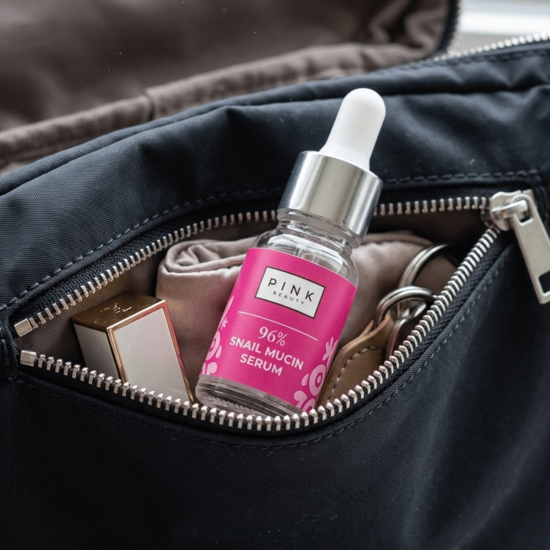 Pink snail mucin serum bottle with dropper in an open black bag.