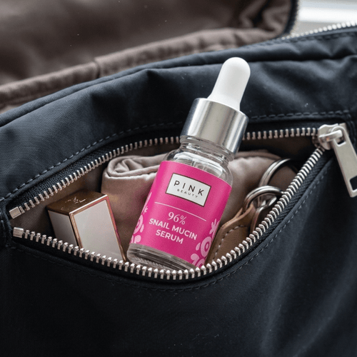 Pink snail mucin serum bottle with dropper in an open black bag.