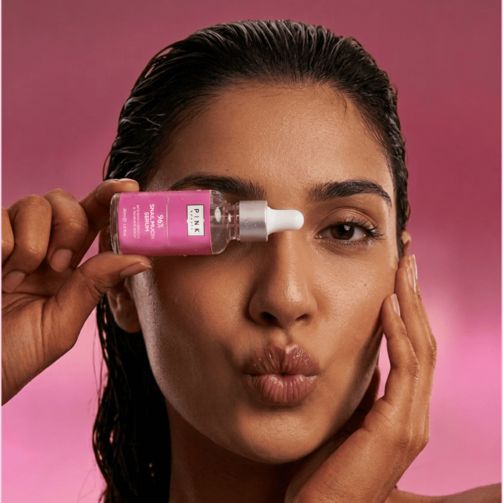 Woman applying a pink skincare product to her face against a pink background