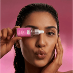 Woman applying a pink skincare product to her face against a pink background