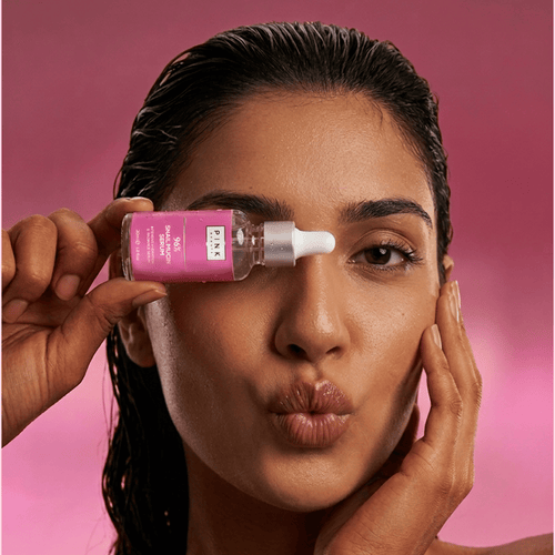 Woman applying a pink skincare product to her face against a pink background