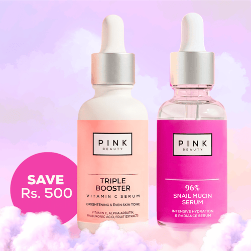 Two Pink Beauty skincare dropper bottles on a pastel pink and purple background with fluffy white cloud props. The left bottle is frosted white with a peach-pink label reading 'PINK BEAUTY TRIPLE BOOSTER VITAMIN C SERUM'.
